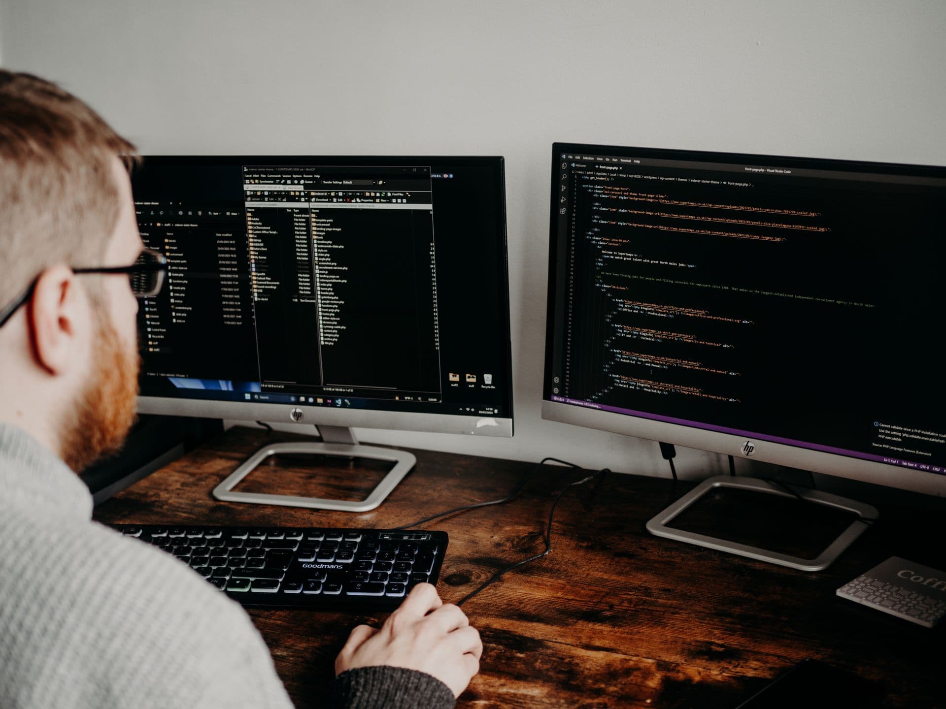 A developer at two monitors, editing front-page.php of a WordPress starter theme in VS Code beside an open SFTP client. Several hero sections carry their image paths inline in style attributes.
